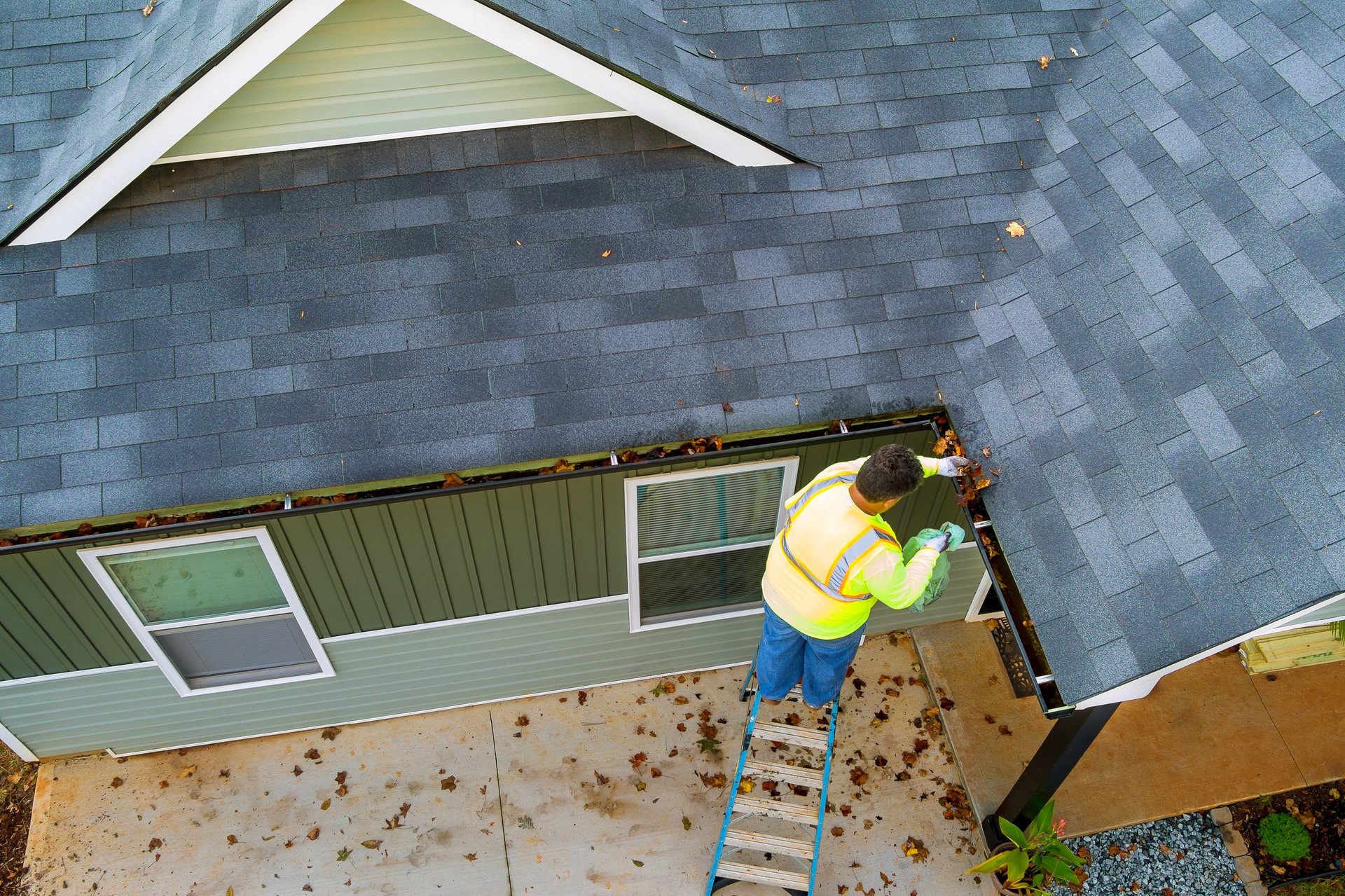 Worker cleaning clogs in roof gutter drain by picking up dirt, debris and fallen leaves