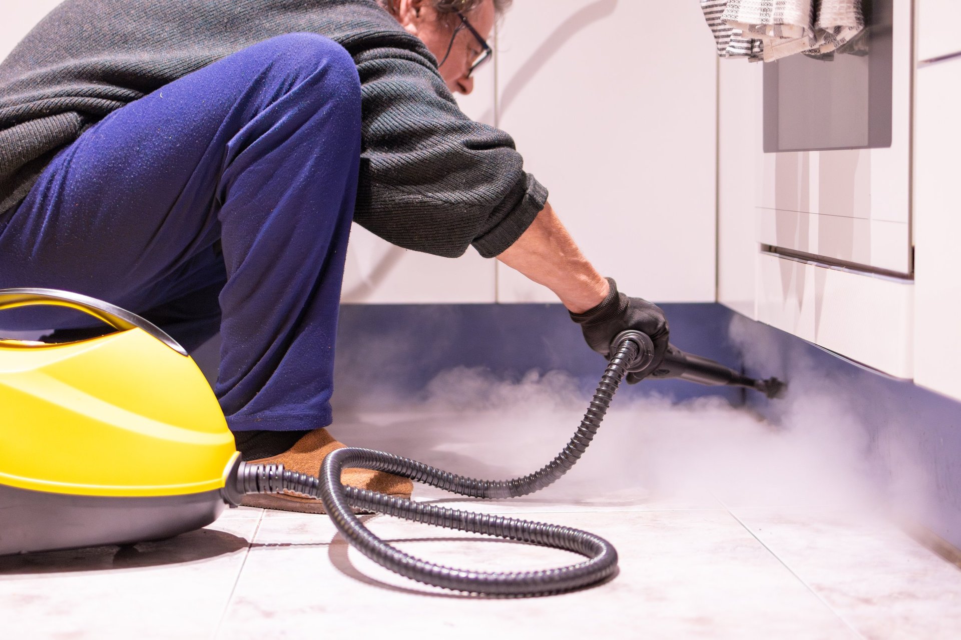 Man crouching down cleaning the house with a steam cleaner appliance