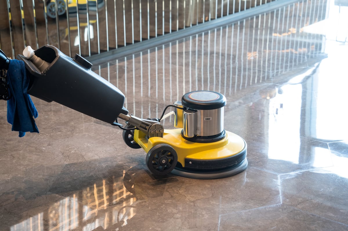 Professional cleaner operating a floor polishing machine to restore a glossy shine to hard flooring