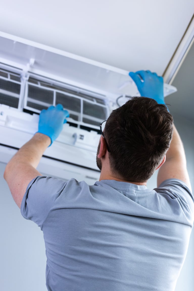 A man wearing blue gloves carefully removes the cover of an air conditioning unit for maintenance