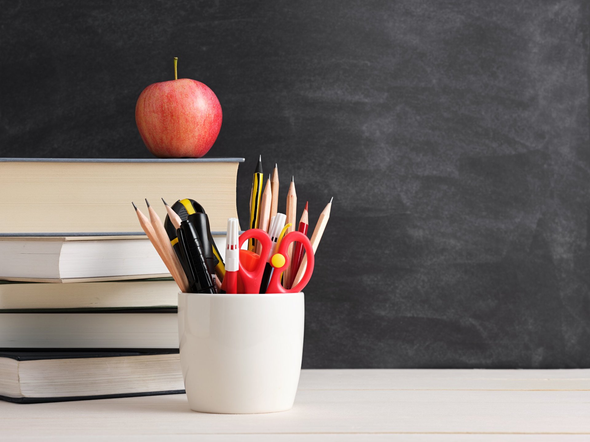 School supplies, books and an apple on a desk against a blackboard, symbolising education