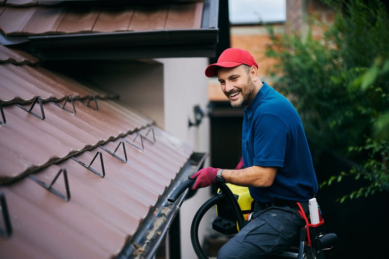 Happy man using leaf blower while cleaning gutters on the roof of a house