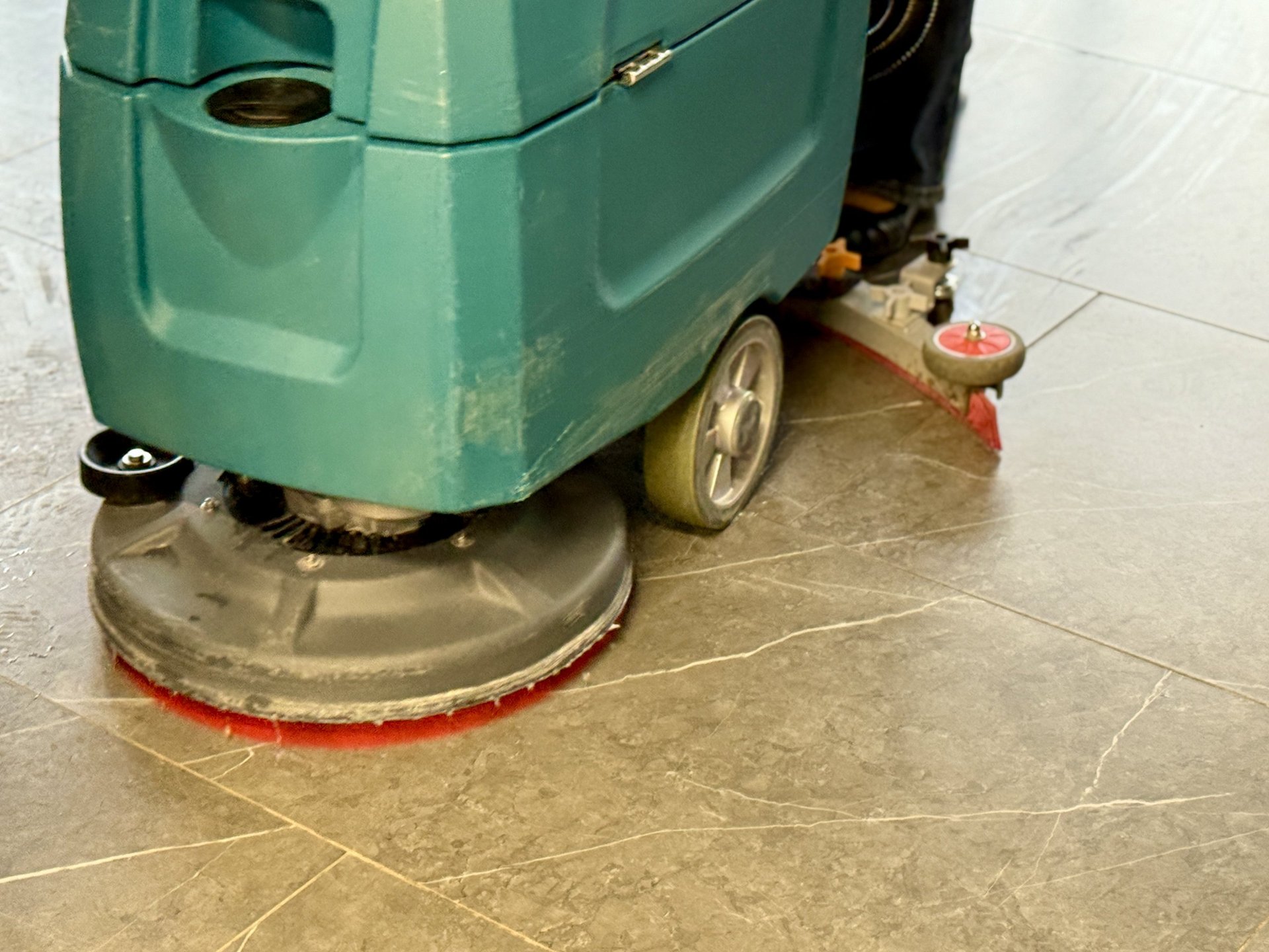 Industrial floor scrubber cleaning shiny tiles inside a corporate lobby, with a wet cleaning path and glossy reflections