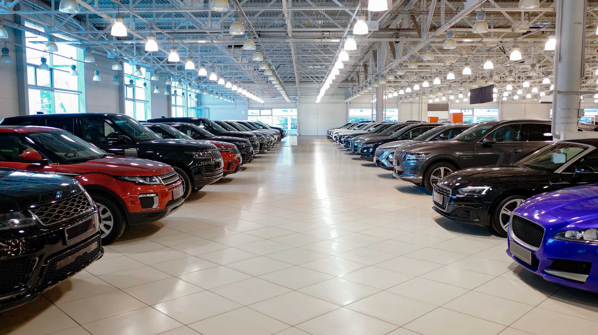Spacious modern car showroom with multiple vehicles parked in rows under bright ceiling lights