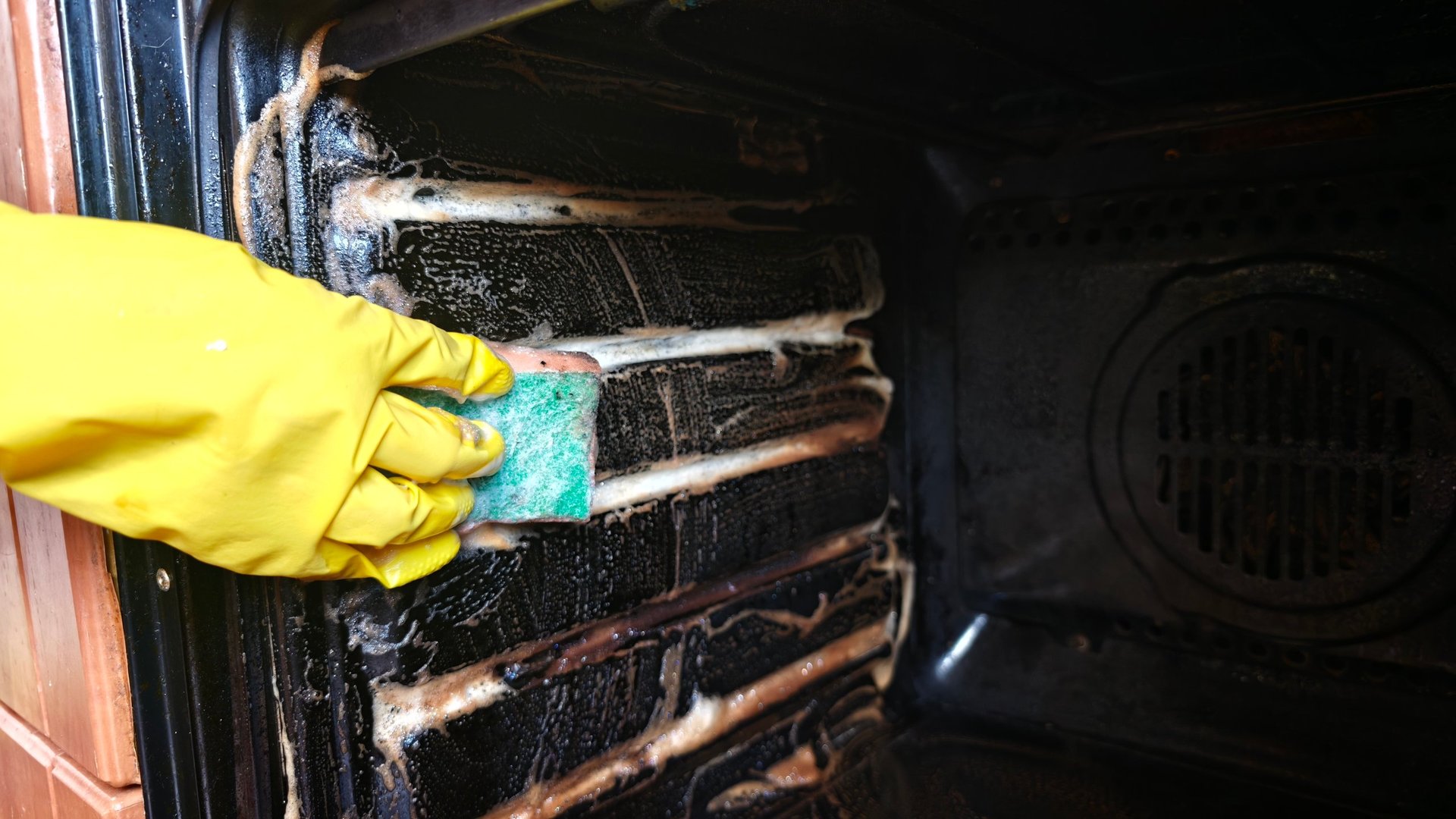 Person cleans the inside of an oven using a sponge and cleaning solution.
