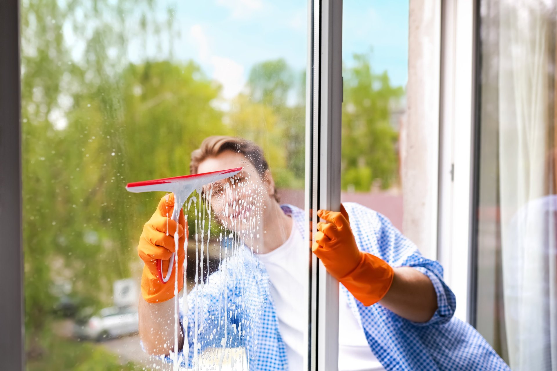 Smiling man washing a glass window with a squeegee and soapy water