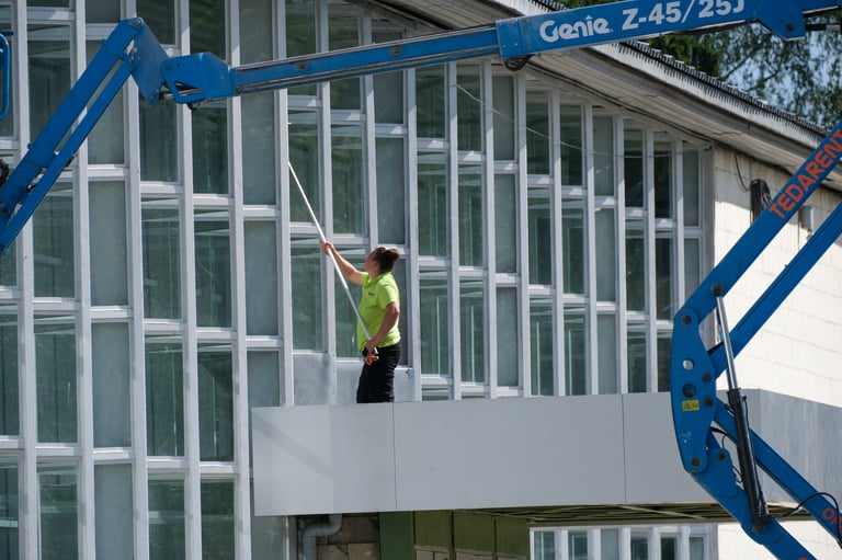 Maintenance worker cleaning the glass facade of a modern building using an extended washing pole