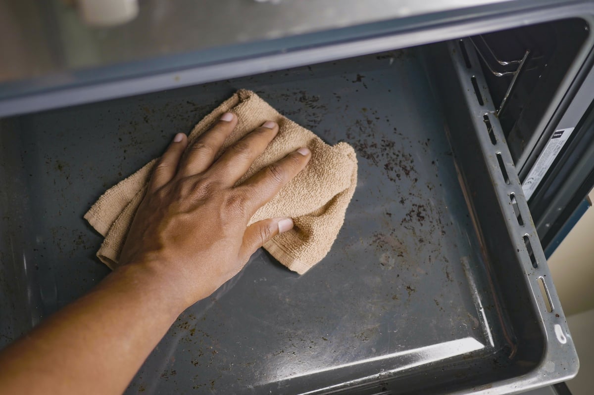 A person wipes a tray in an oven with a cloth at home.